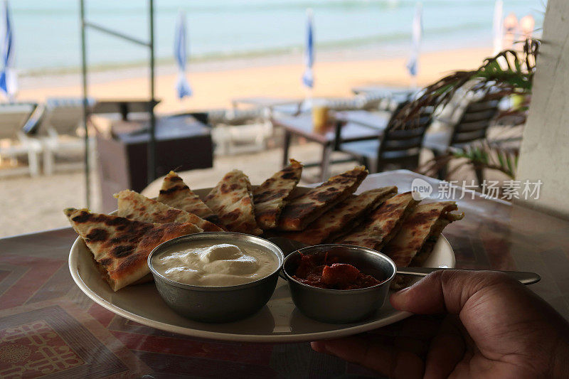 印度自助早餐的形象，三角形的aloo paratha切片和焦糖洋葱撒，白色盘子由一个不认识的人，美味的面包塞满了garam masala土豆，酒店餐厅aloo paratha菜，raita凝乳酸奶